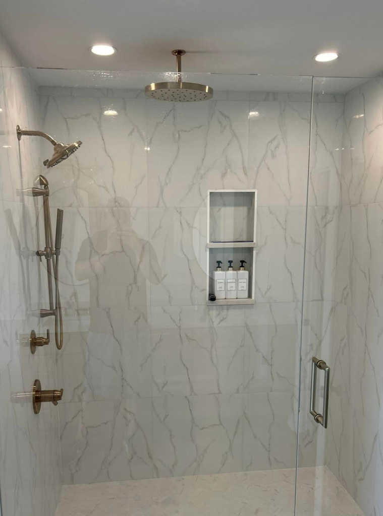 Remodeled bathroom shower with marble tile, silver fixtures and glass door.
